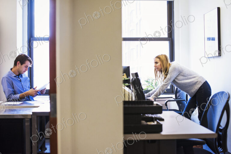 A shot of a young man sitting in an office looking at a cellphone, and a young woman…
