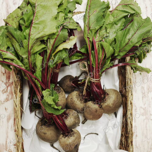 A shot of bundles of beets in a basket on a wooden surface, seen from above.