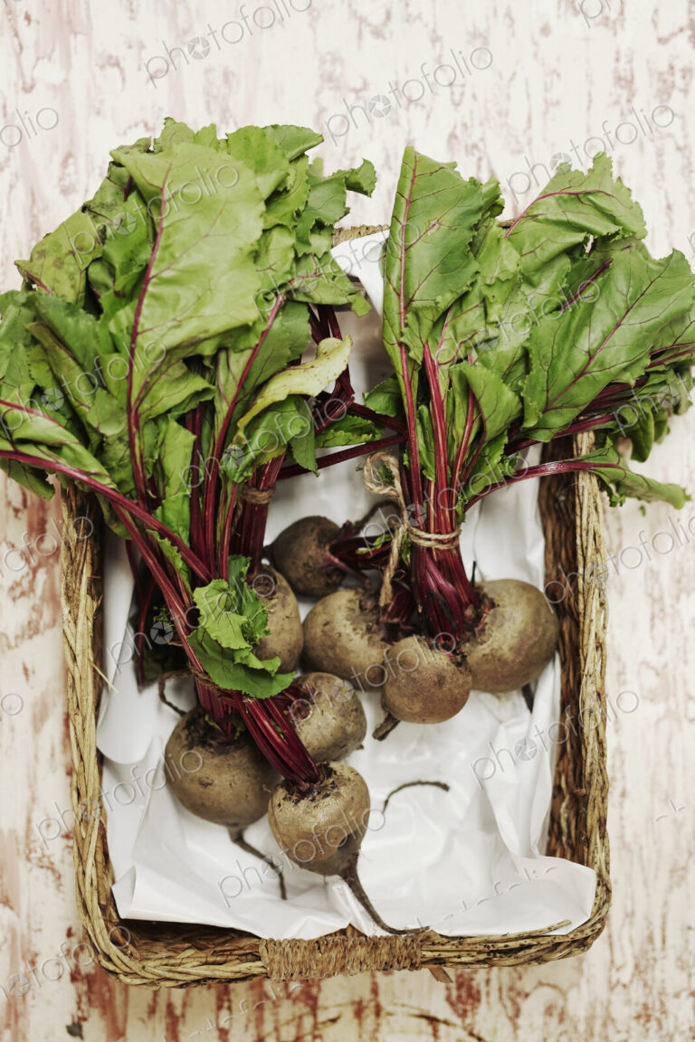 A shot of bundles of beets in a basket on a wooden surface, seen from above.