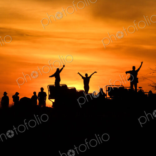 A silhouette of people and a vehicle, people with hands in the air, against sunset,… A silhouette of people and a vehicle, people with hands in the air, against sunset,…