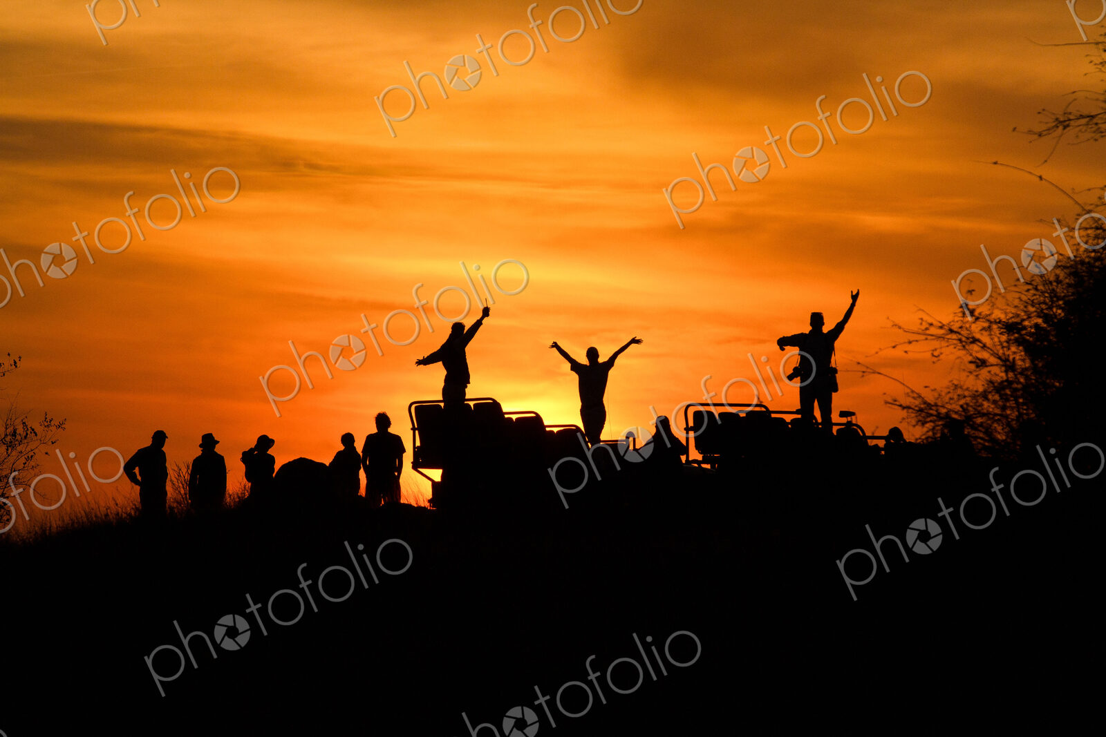 A silhouette of people and a vehicle, people with hands in the air, against sunset,…