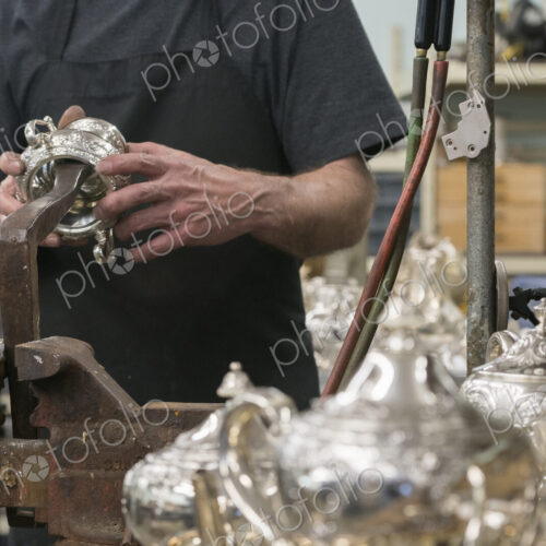 A silversmith in his workshop holding a silver pot examining it. A silversmith in his workshop holding a silver pot examining it.