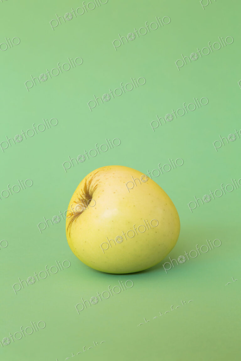 A single Golden Delicious apple on a green background.