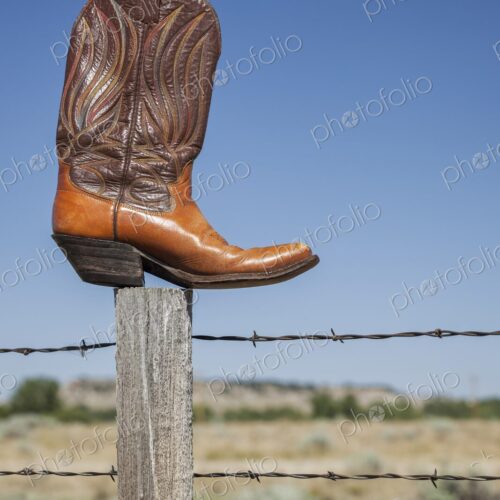 A single cowboy boot rests on a fence post against a clear blue sky in Wyoming. Symbol… A single cowboy boot rests on a fence post against a clear blue sky in Wyoming. Symbol…