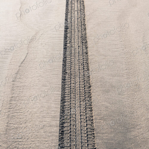 A single tyre track on wet sand, on a beach
