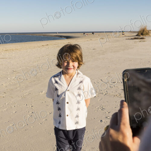 A six year old boy being photographed by his mother at the beach