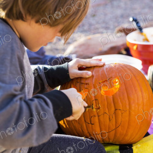 A six year old boy carving pumpkin outdoors at Halloween.