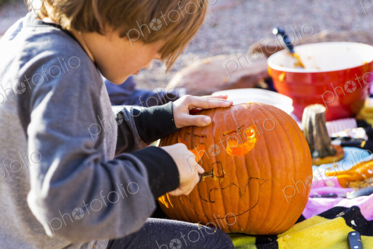 A six year old boy carving pumpkin outdoors at Halloween.