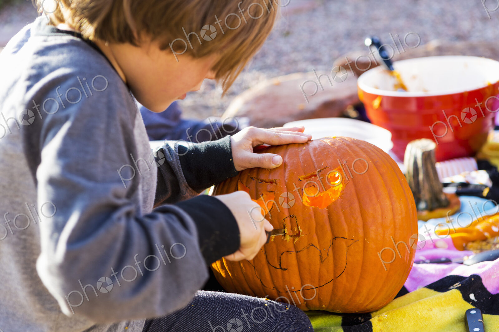 A six year old boy carving pumpkin outdoors at Halloween.