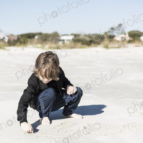A six year old boy drawing in the soft white sand on the beach A six year old boy drawing in the soft white sand on the beach