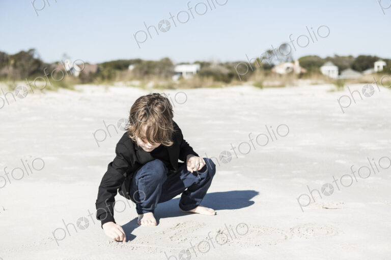 A six year old boy drawing in the soft white sand on the beach