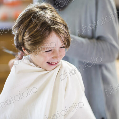 A six year old boy getting his hair cut at home by his mother A six year old boy getting his hair cut at home by his mother