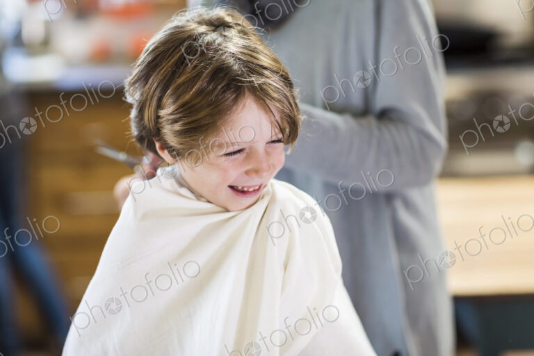A six year old boy getting his hair cut at home by his mother