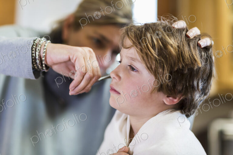 A six year old boy getting his hair cut at home by his mother