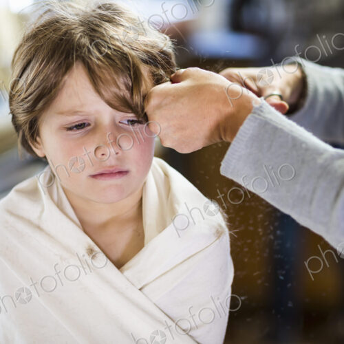 A six year old boy getting his hair cut at home by his mother