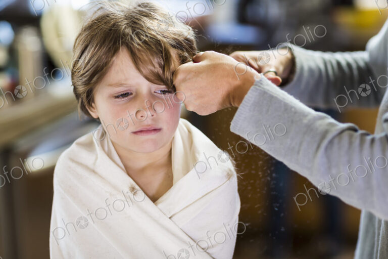 A six year old boy getting his hair cut at home by his mother