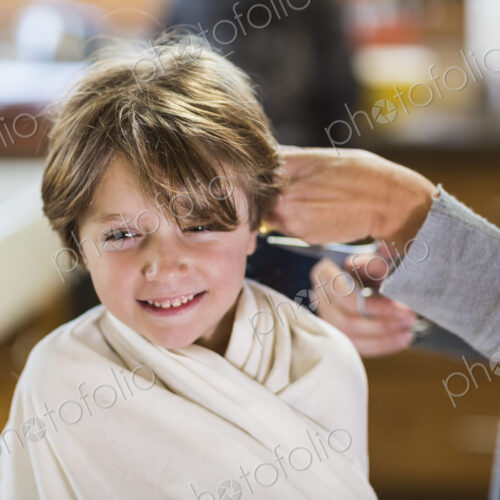 A six year old boy getting his hair cut at home by his mother