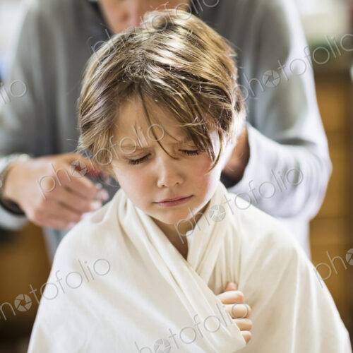 A six year old boy getting his hair cut at home by his mother A six year old boy getting his hair cut at home by his mother