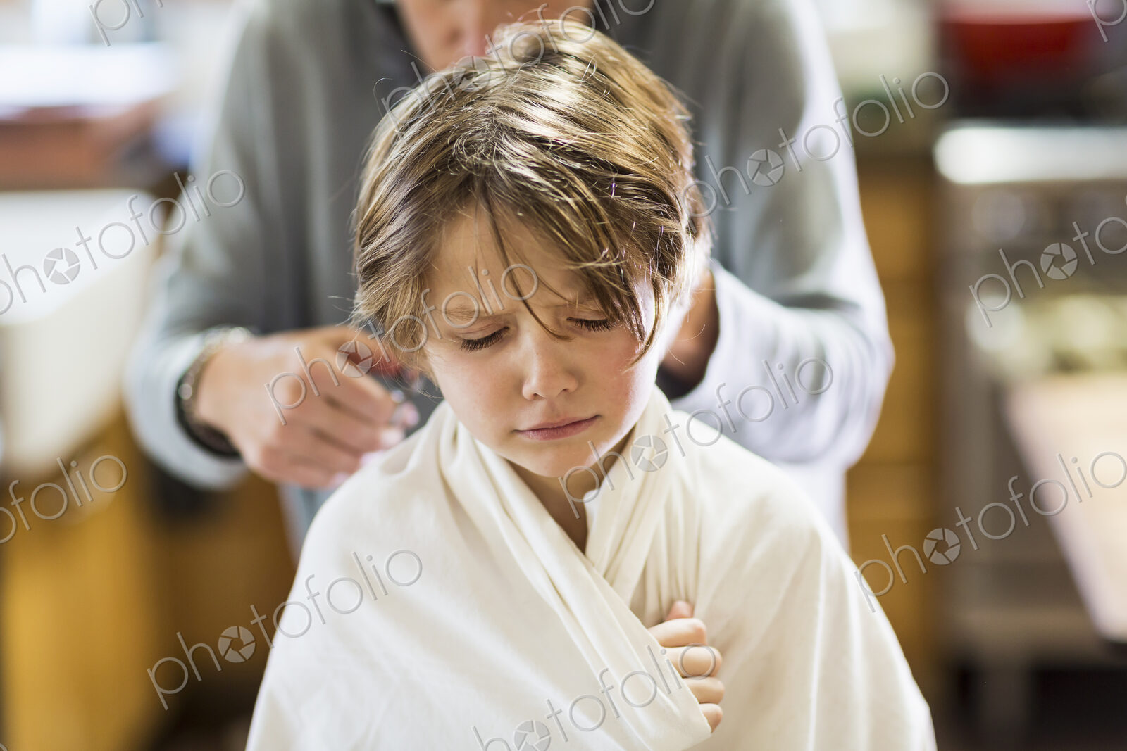 A six year old boy getting his hair cut at home by his mother