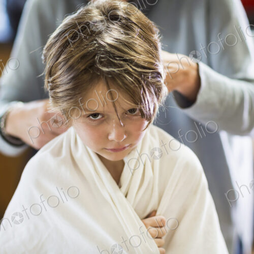 A six year old boy getting his hair cut at home by his mother A six year old boy getting his hair cut at home by his mother