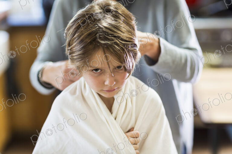 A six year old boy getting his hair cut at home by his mother