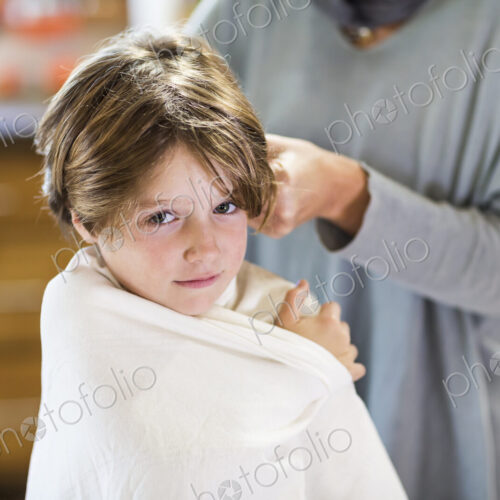 A six year old boy getting his hair cut at home by his mother