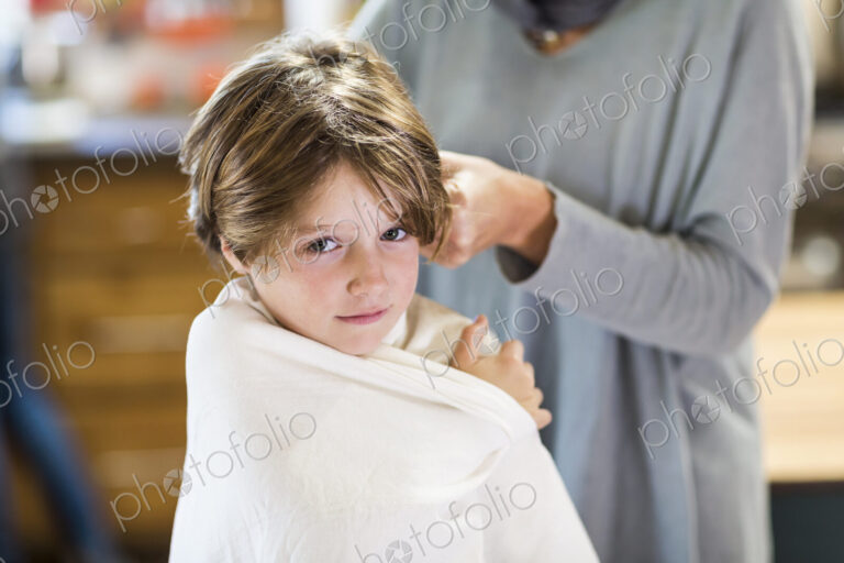 A six year old boy getting his hair cut at home by his mother