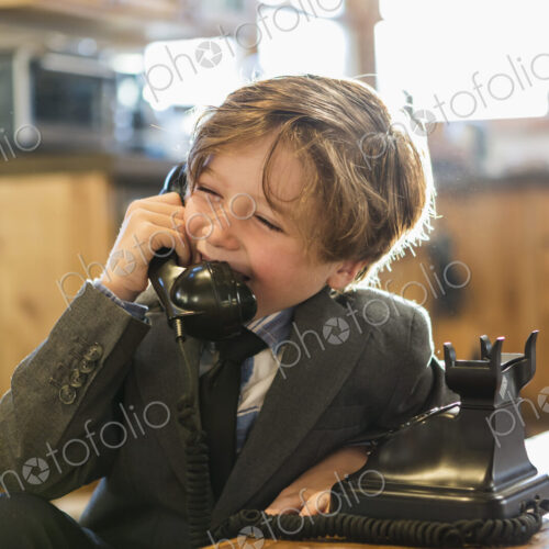 A six year old boy in a suit and tie talking on a old vintage phone at home A six year old boy in a suit and tie talking on a old vintage phone at home
