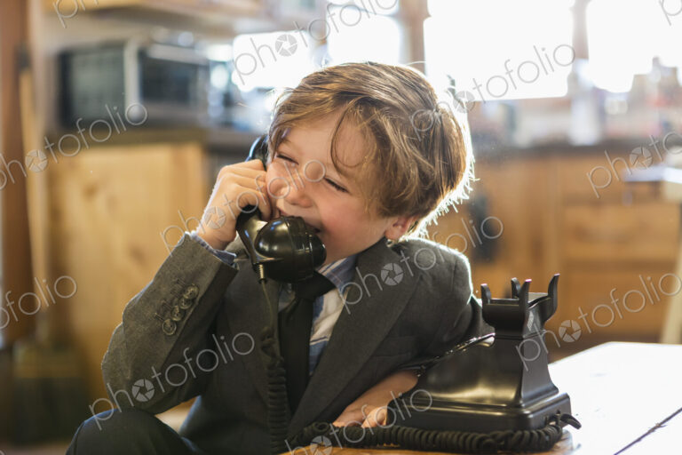A six year old boy in a suit and tie talking on a old vintage phone at home