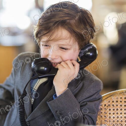 A six year old boy in a suit talking on a old vintage phone at home A six year old boy in a suit talking on a old vintage phone at home