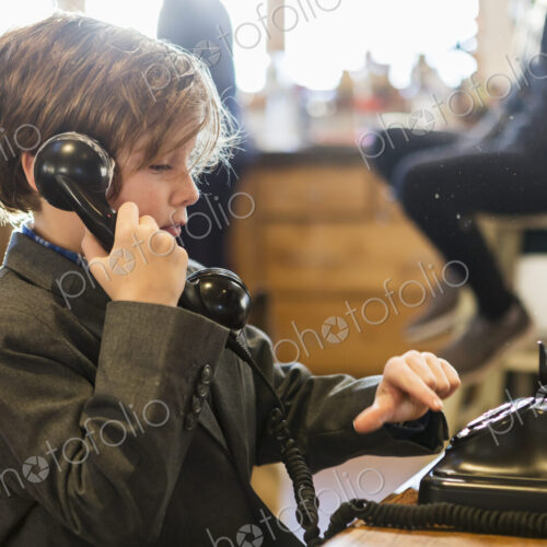 A six year old boy in a suit talking on a old vintage phone at home