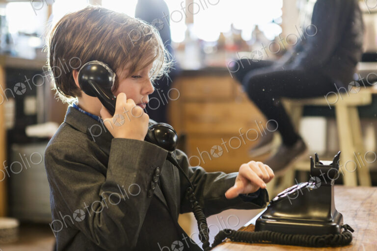 A six year old boy in a suit talking on a old vintage phone at home