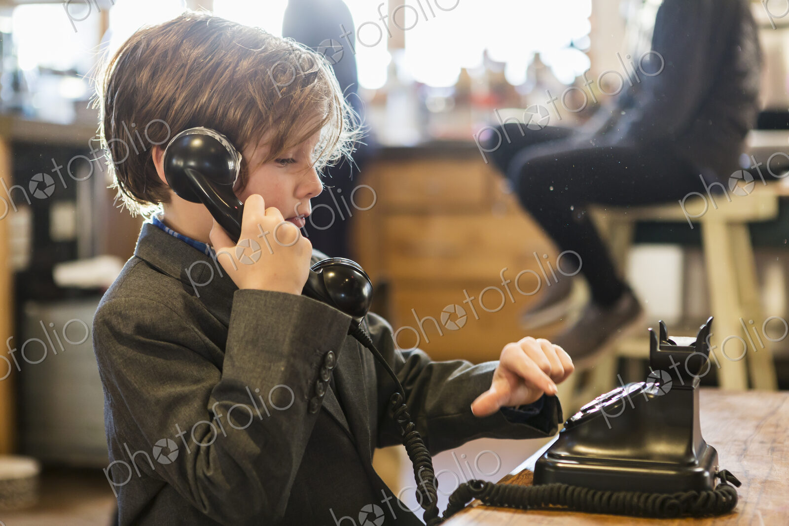 A six year old boy in a suit talking on a old vintage phone at home