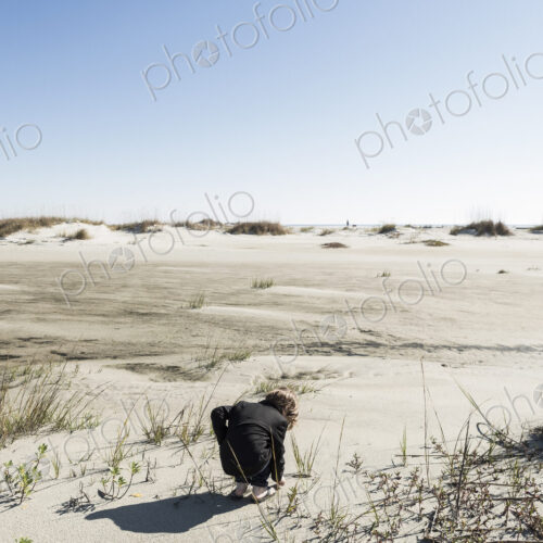 A six year old boy in soft white sand dunes, bending down to inspect something. A six year old boy in soft white sand dunes, bending down to inspect something.