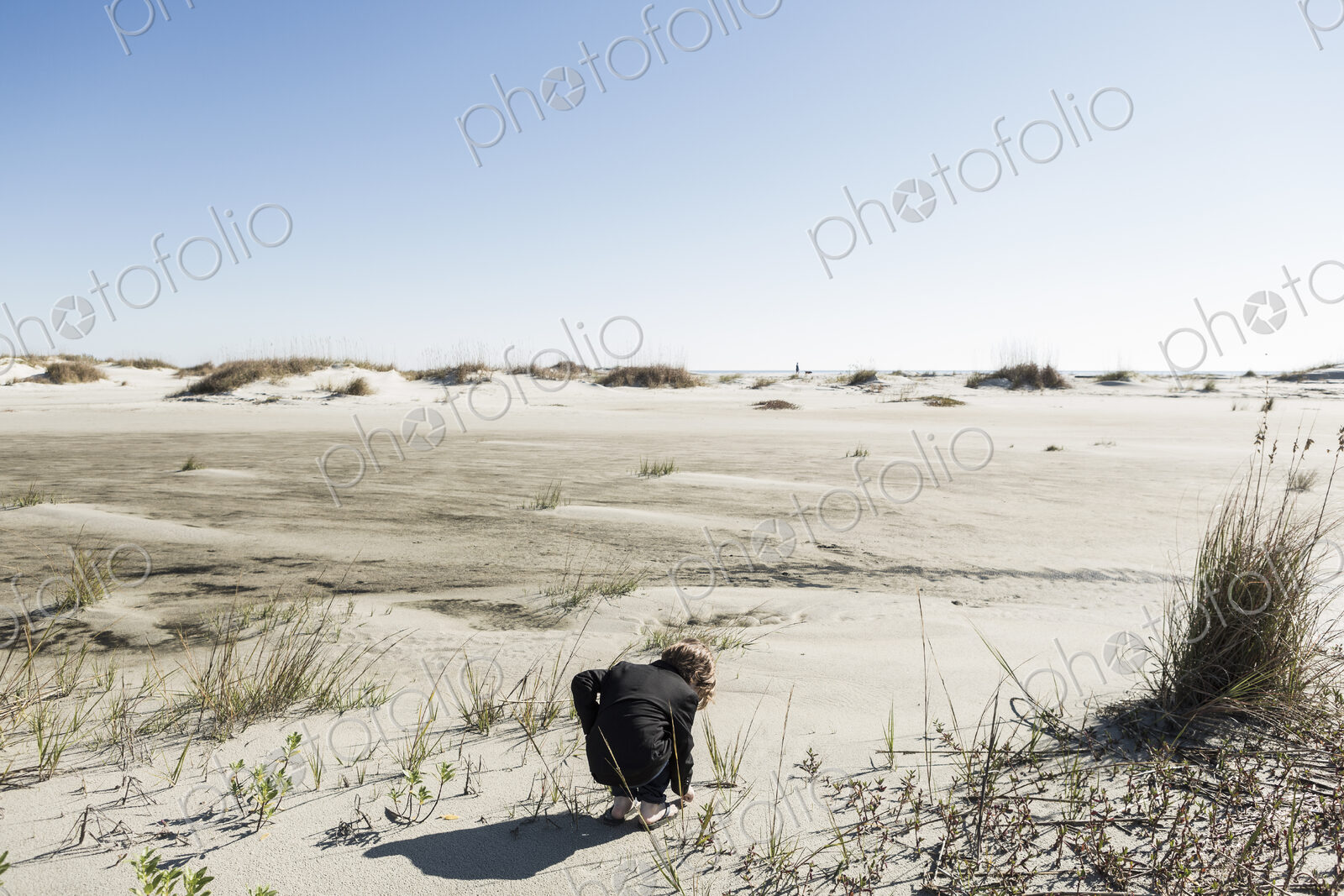 A six year old boy in soft white sand dunes, bending down to inspect something.