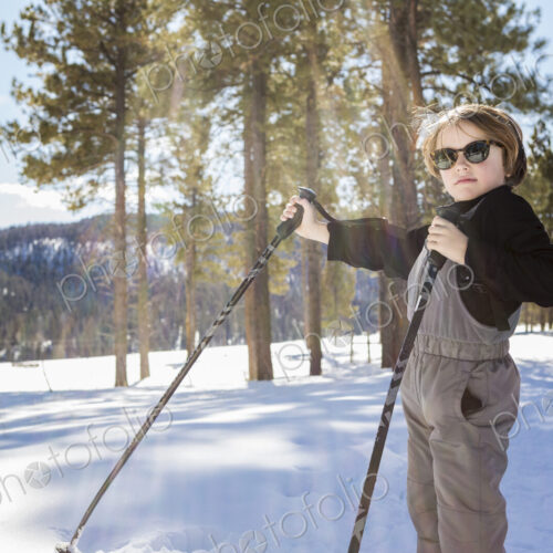 A six year old boy in woodland holding ski poles