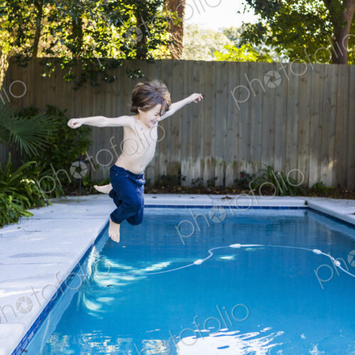 A six year old boy leaping into a swimming pool