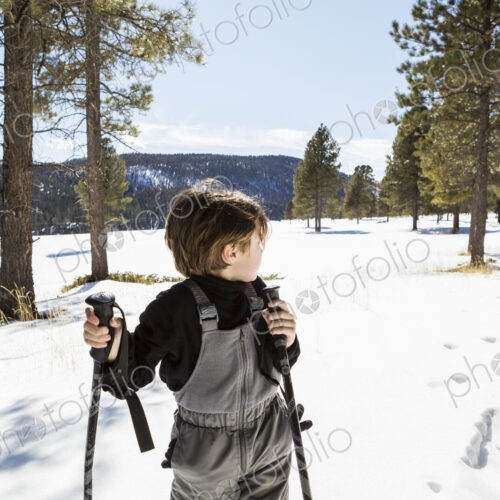 A six year old boy on snow shoes among trees.