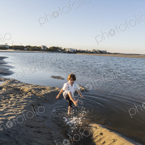 A six year old boy on the beach splashing in shallow water A six year old boy on the beach splashing in shallow water