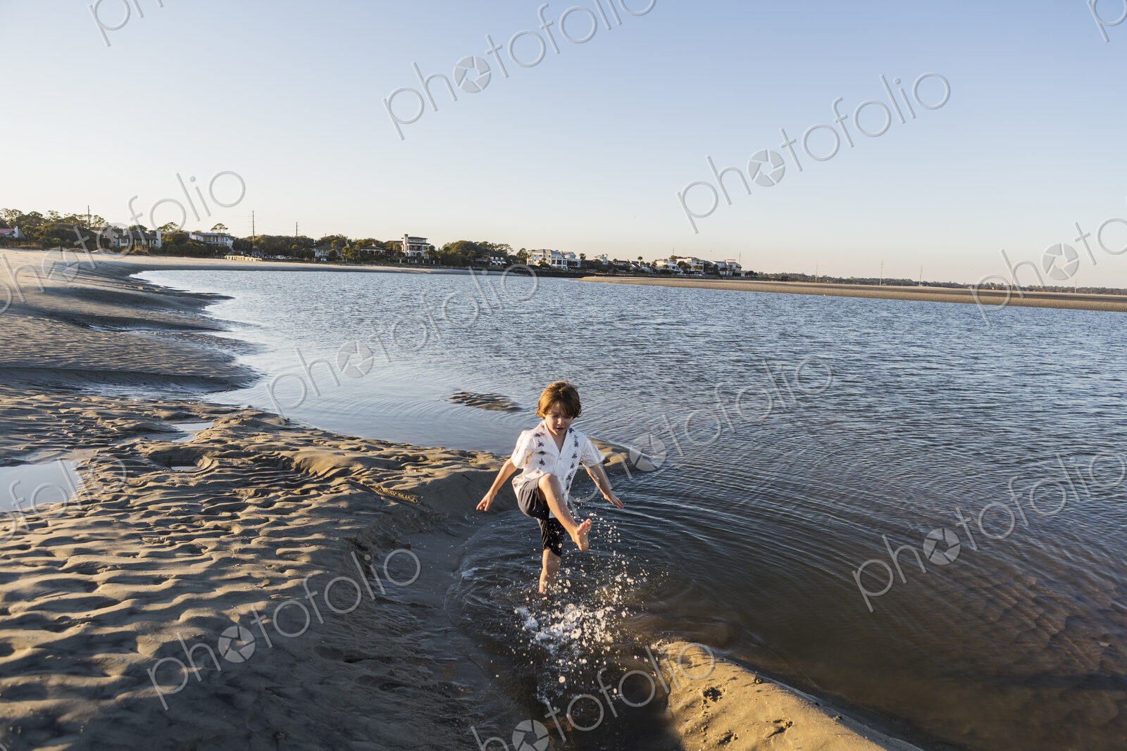 A six year old boy on the beach splashing in shallow water