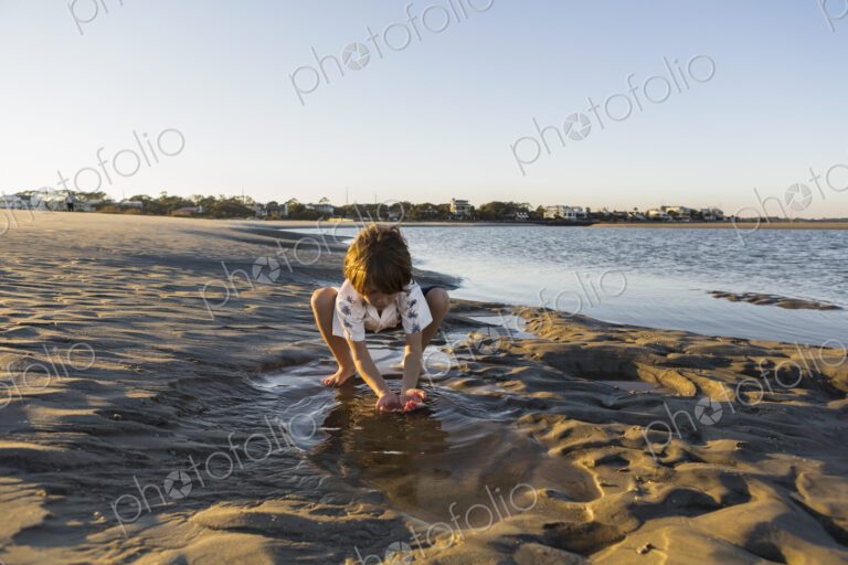 A six year old boy playing on the beach in a pool of water