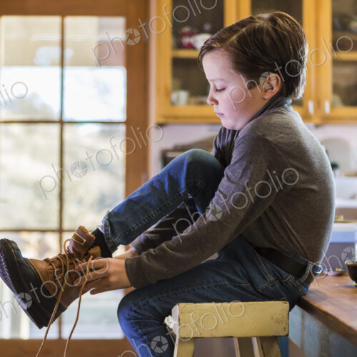 A six year old boy putting his boots on, sitting on a high stool. A six year old boy putting his boots on, sitting on a high stool.