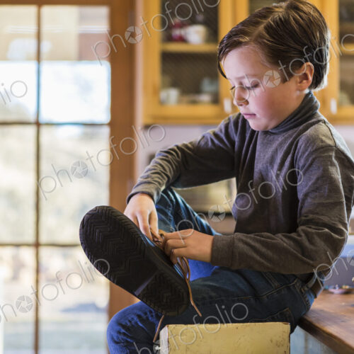 A six year old boy putting his boots on, sitting on a high stool. A six year old boy putting his boots on, sitting on a high stool.