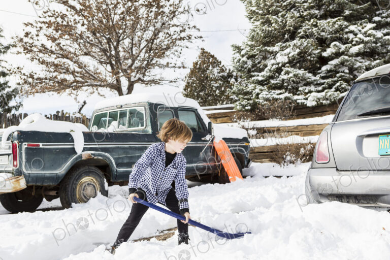 A six year old boy shoveling snow in driveway