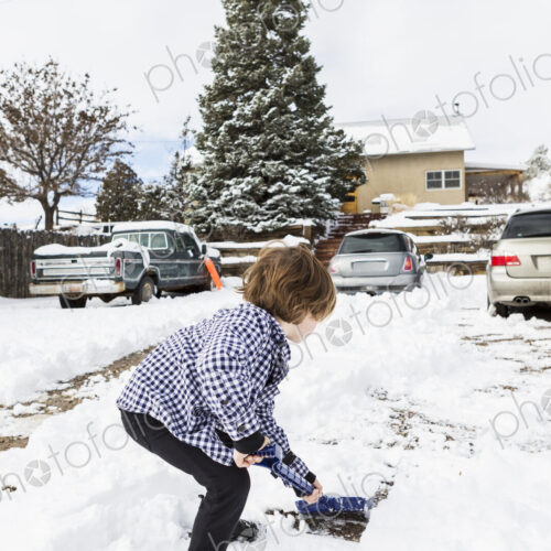 A six year old boy shoveling snow in driveway