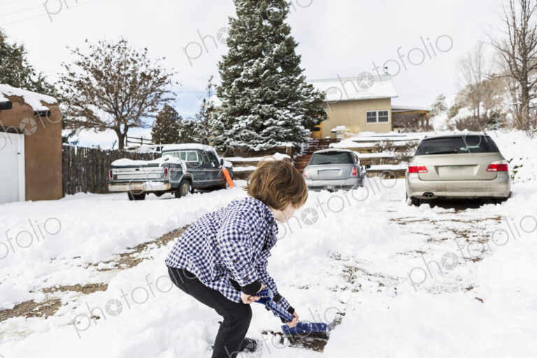 A six year old boy shoveling snow in driveway