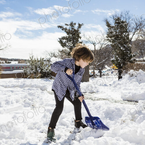 A six year old boy shoveling snow in driveway