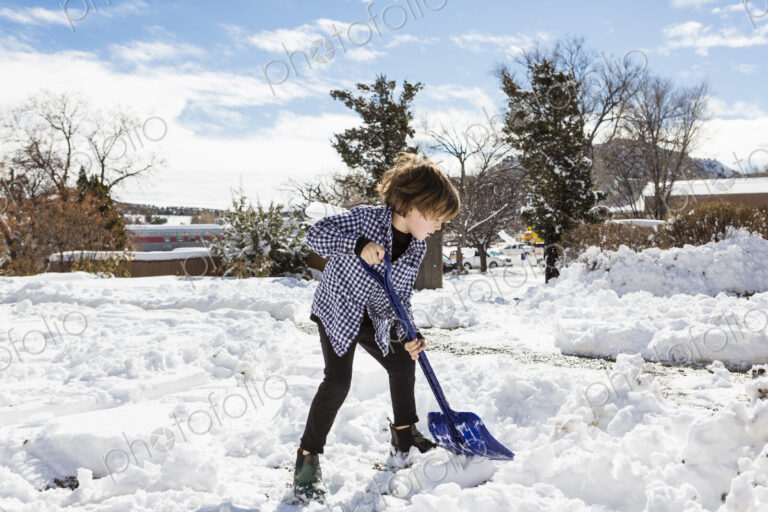 A six year old boy shoveling snow in driveway