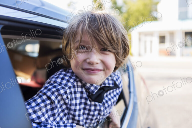 A six year old boy smiling at camera, looking out of car window