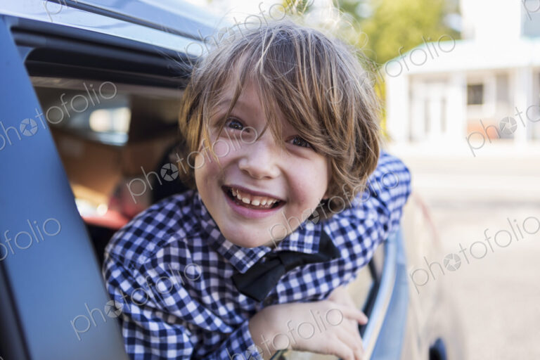 A six year old boy smiling at camera, looking out of car window